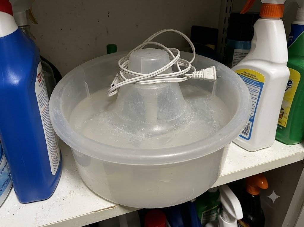 An abandoned plastic cat fountain with hazy scratched plastic, unplugged on a storage shelf